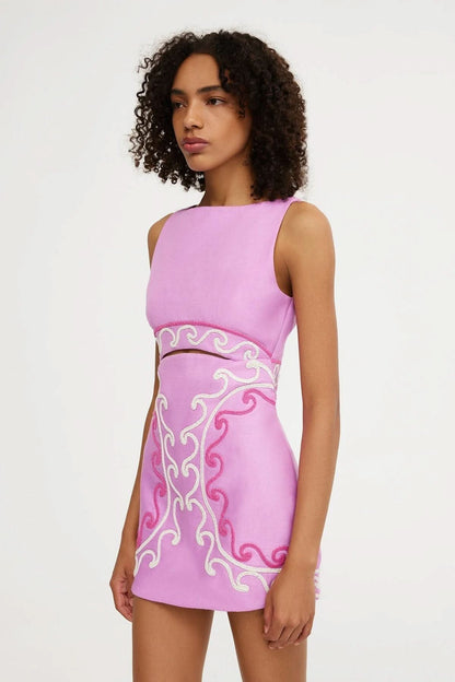 Side view of pink cut-out mini dress with cream and magenta embroidered scrolls