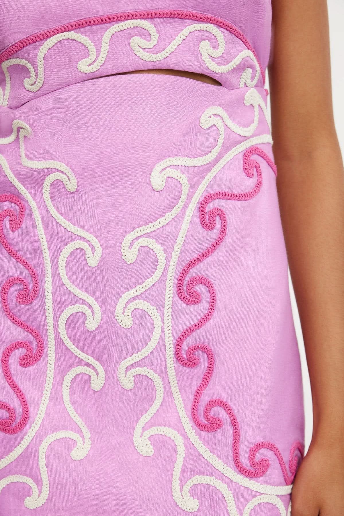 Close-up of ornate cream and pink embroidered scroll detailing on pink dress fabric