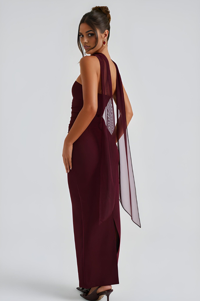 Side view of burgundy strapless maxi dress with draped sheer scarf accent
